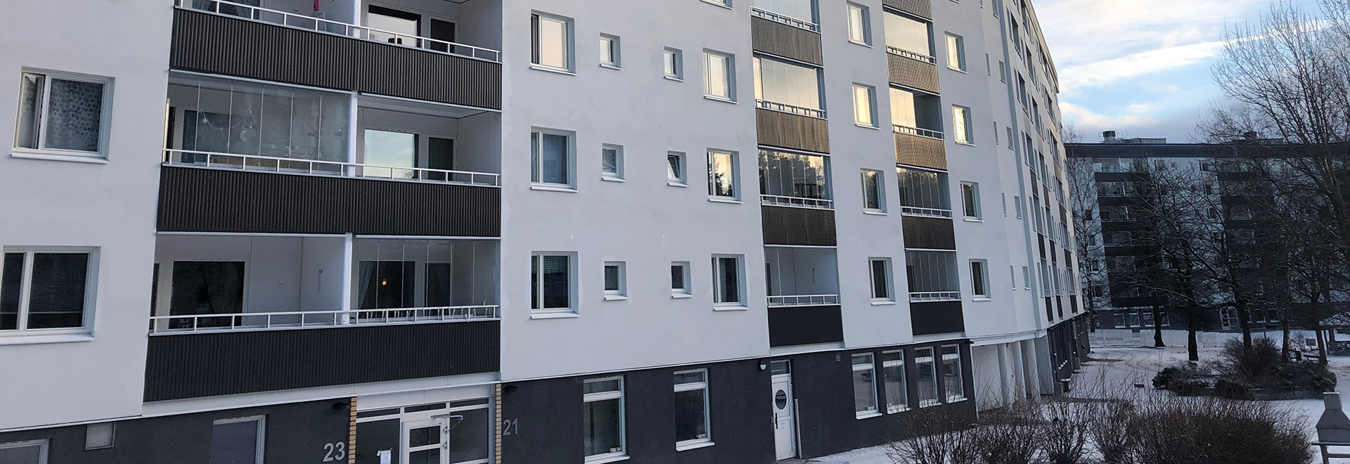 Vit putsad fasad med grå sockel på flerbostadshus